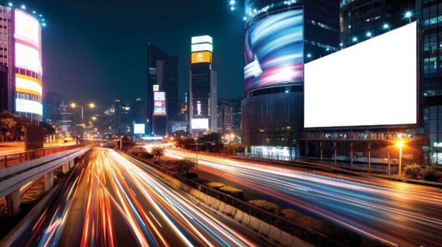 A view of a city bustling with car lights and billboards.