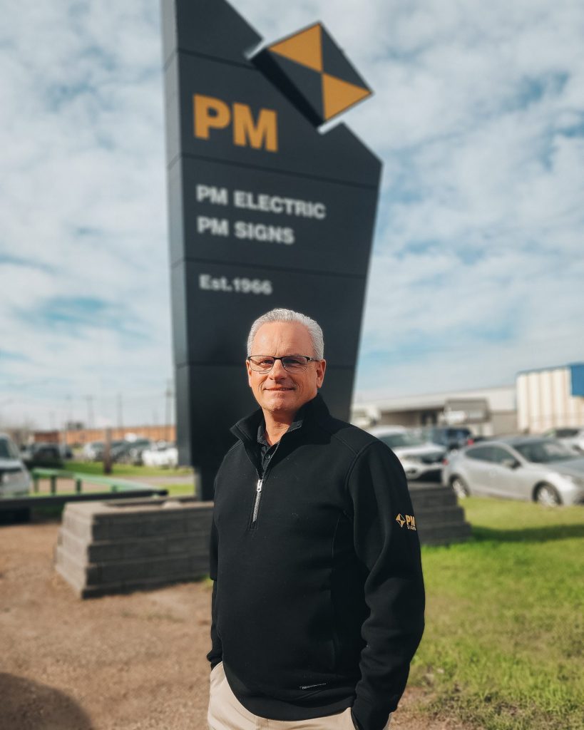 A headshot of Erik Houde in front of a PM Signs sign.