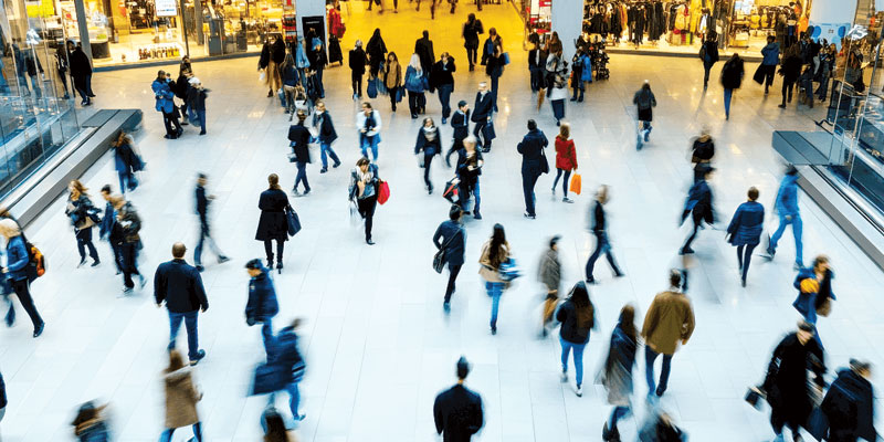 People walk by a busy indoor mall/shopping centre.