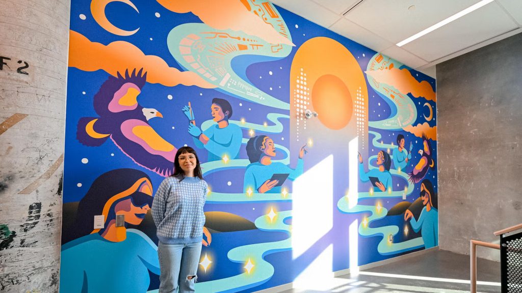 The artist stands next to the mural painted by her.