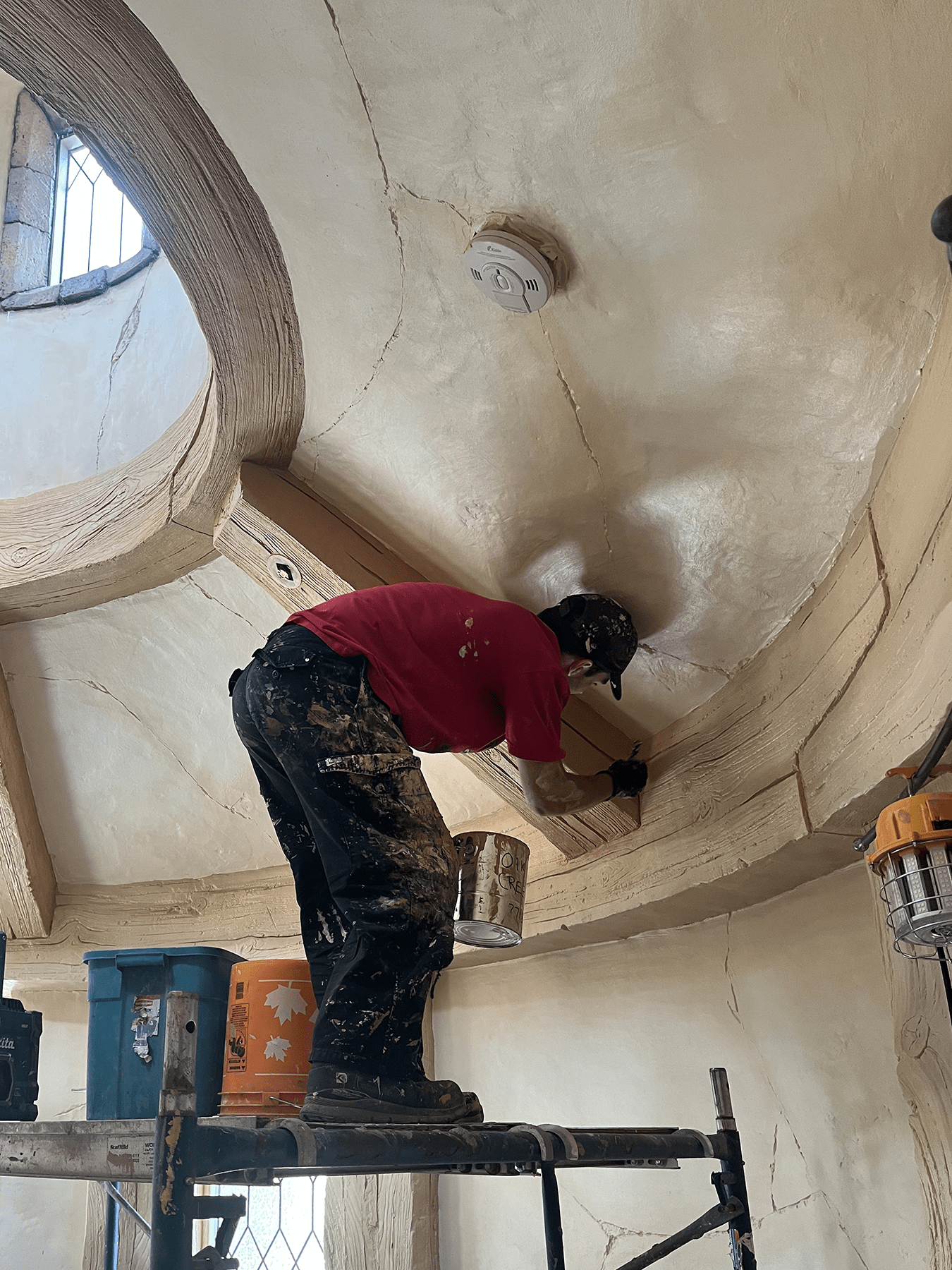 Worker hand-finishing a curved plaster ceiling inside a fantasy-themed room under construction, standing on scaffolding