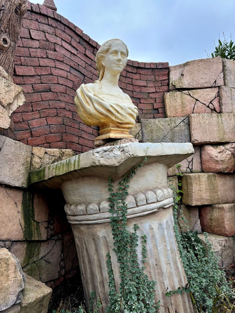 Bust on a fluted stone pedestal surrounded by crumbling brick walls and ivy