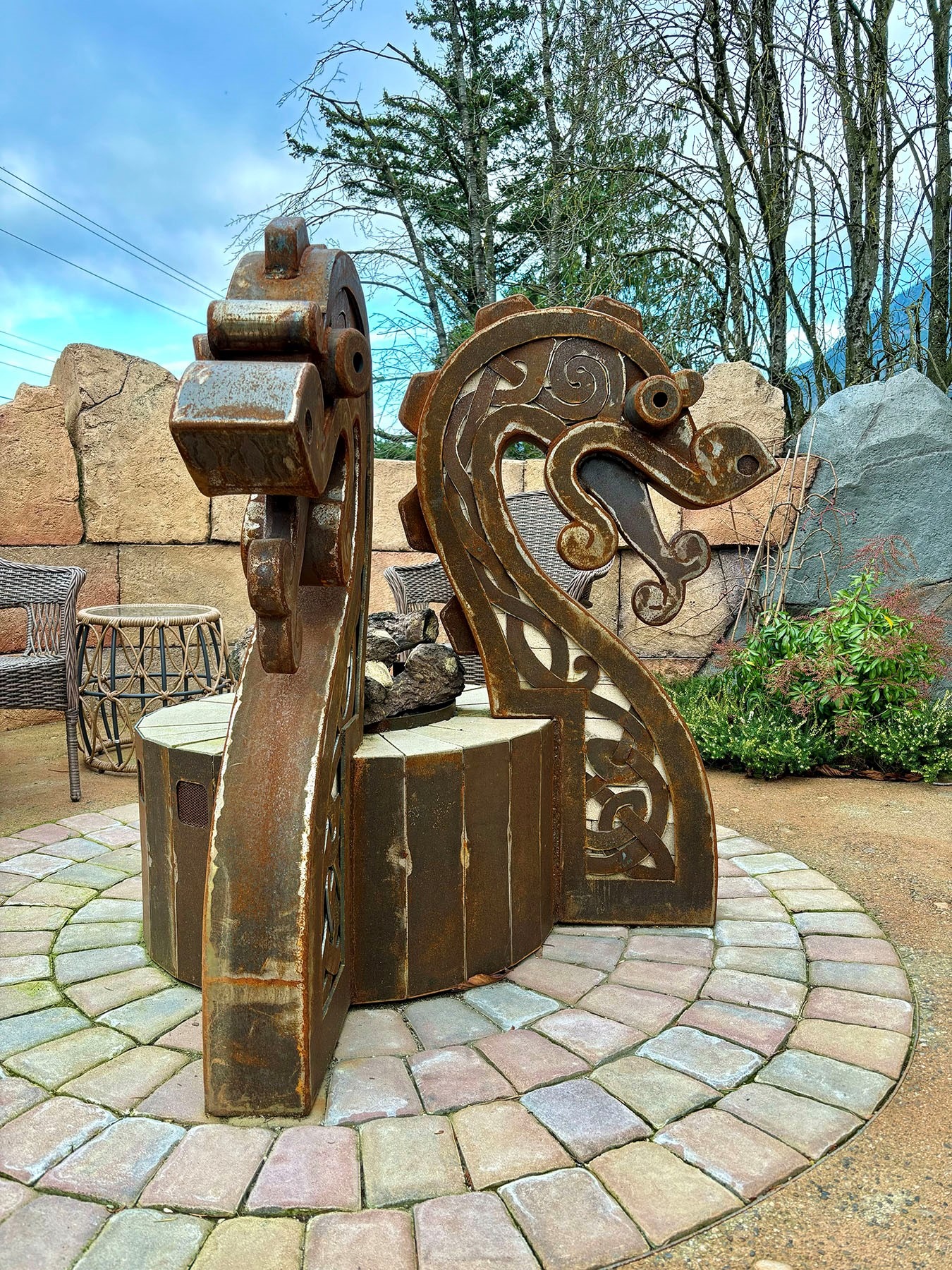 Large rustic metal sculpture with Celtic scroll cutwork on a circular cobblestone patio