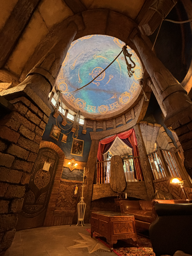 Interior of a fantasy-themed tower room with a painted celestial dome ceiling and stone arched walls