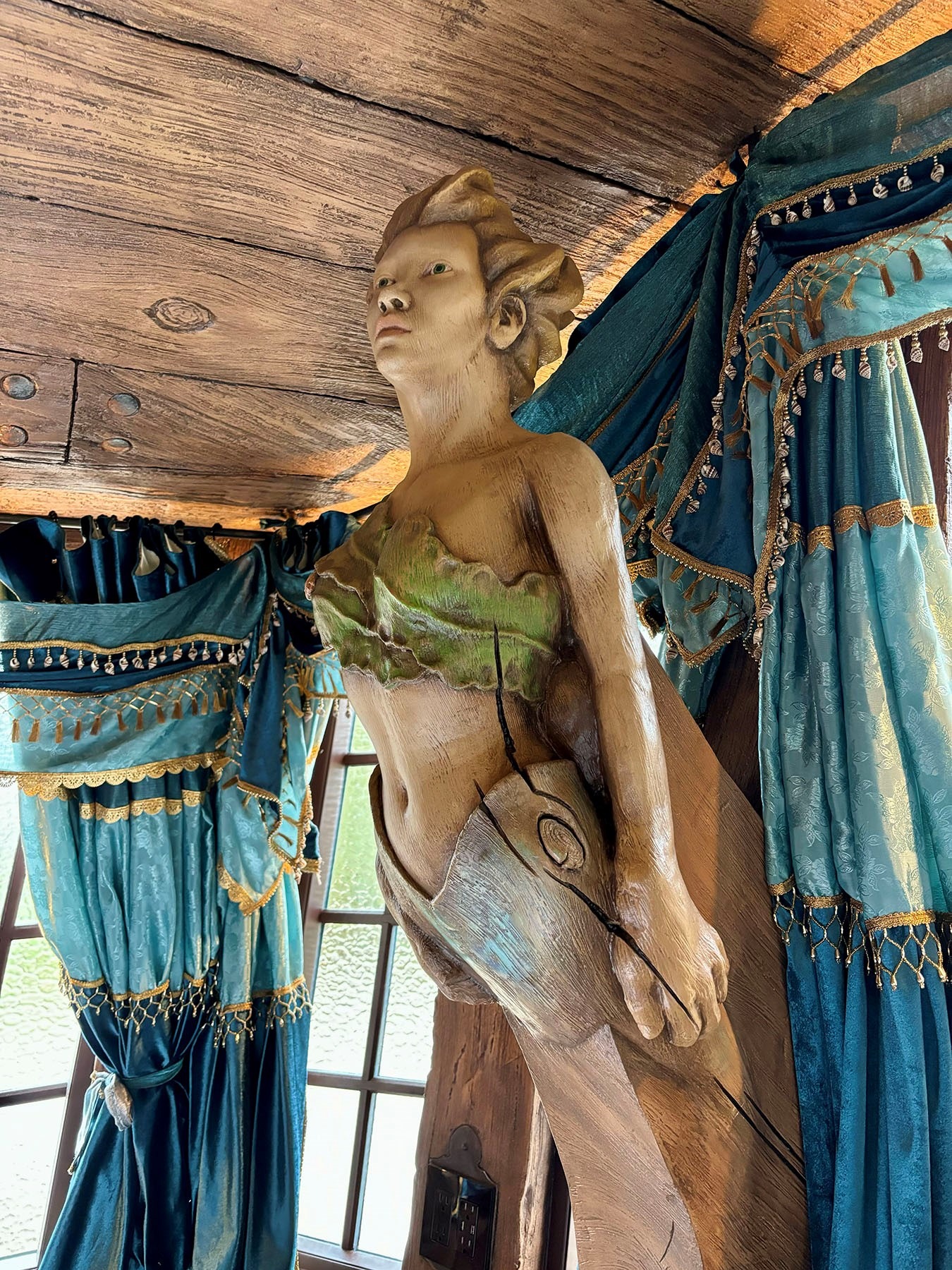 Carved wooden ship figurehead of a female figure displayed against teal nautical curtains
