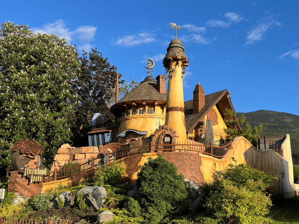 Exterior of Hazelnut Inn, a whimsical yellow stucco building with turrets and a forested mountain backdrop