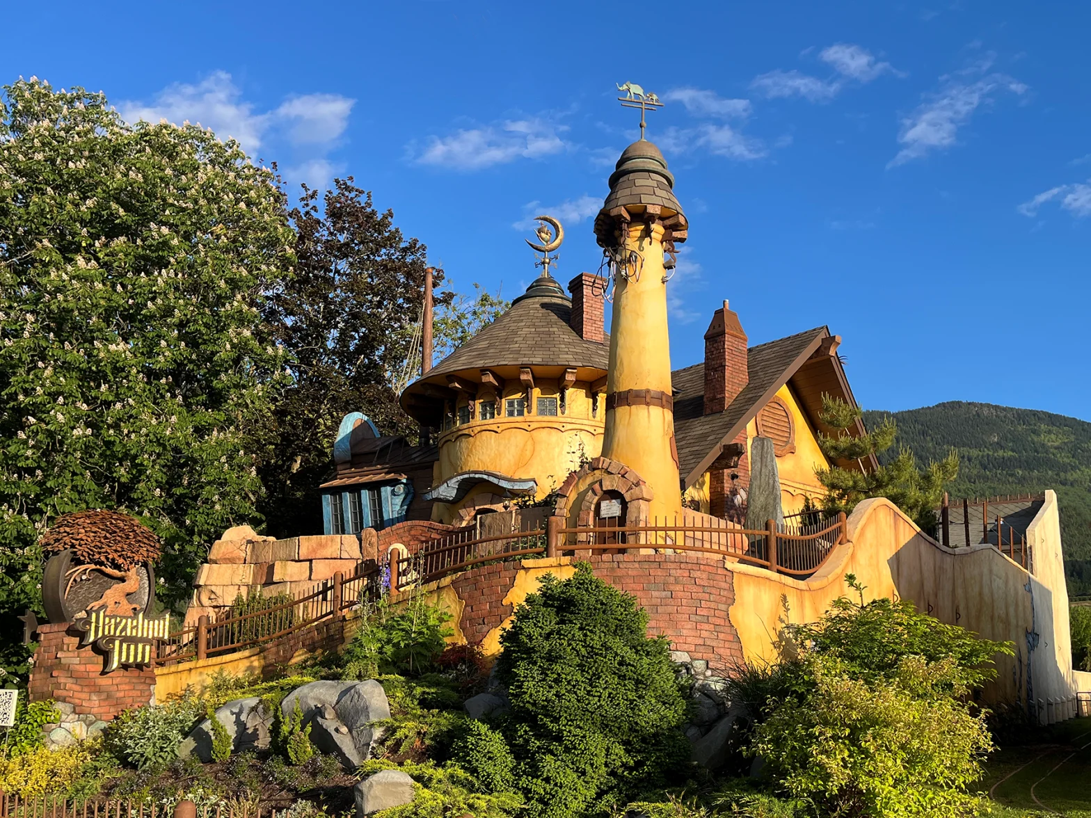 Exterior of Hazelnut Inn, a whimsical yellow stucco building with turrets and a forested mountain backdrop