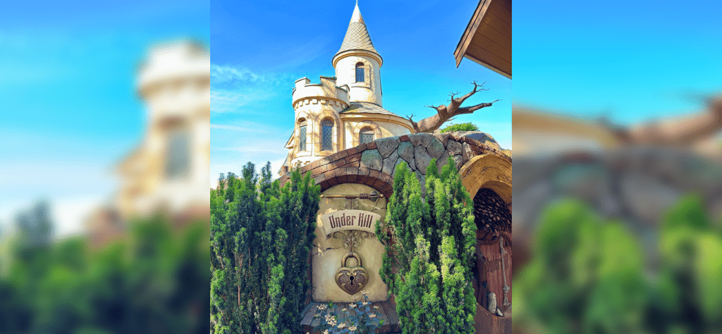 "Under Hill" sign with a heart padlock motif set into a stone arch, with a fantasy castle turret in the background