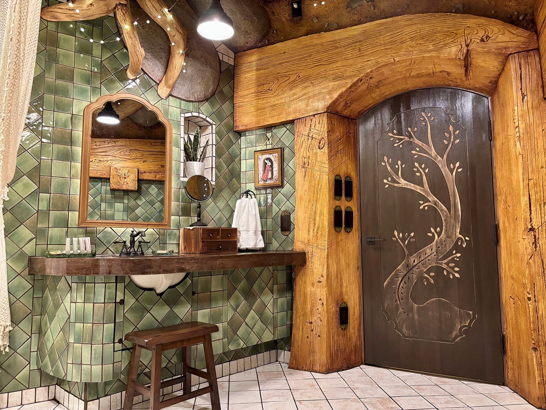 Fantasy-themed bathroom with green diamond tile, wood-framed mirror, vessel sink, and a dark door carved with a tree motif