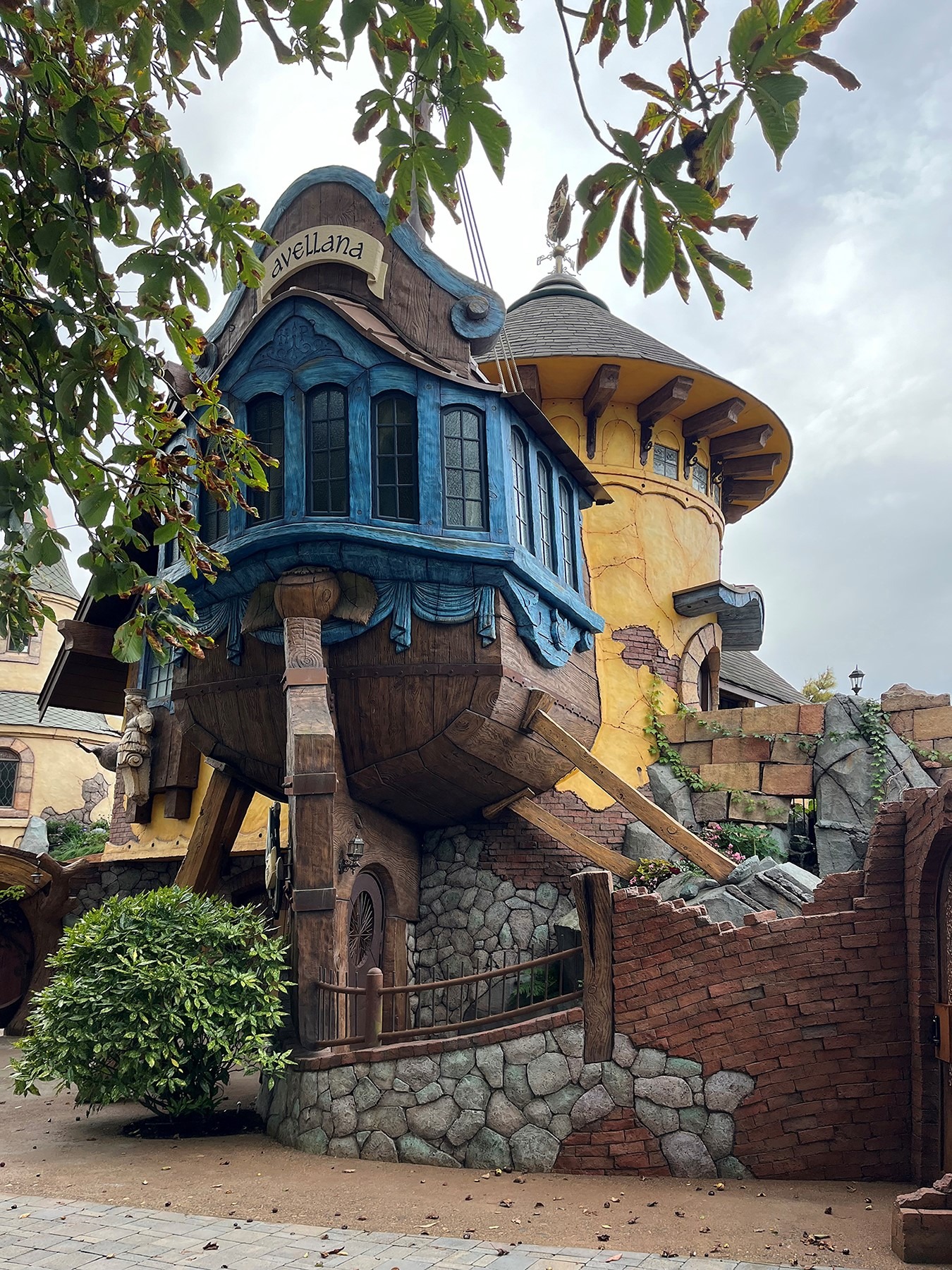 Avellana fantasy-themed building with a blue ship-hull upper floor elevated on timber posts next to a yellow stucco tower