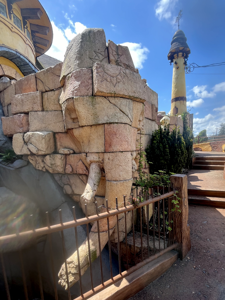 Stone elephant sculpture at a fantasy-themed attraction with a lighthouse tower in the background