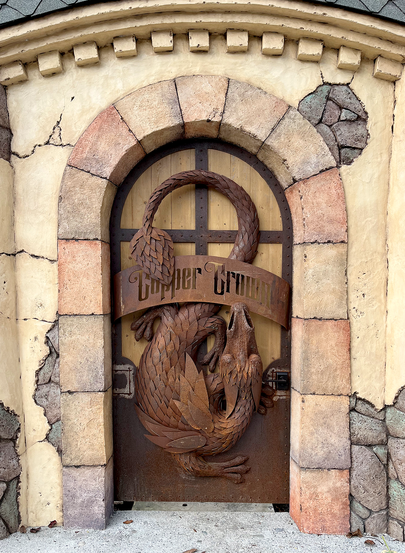 Arched wooden door to Copper Crown featuring a large sculpted metal dragon wrapped around a "Copper Crown" banner