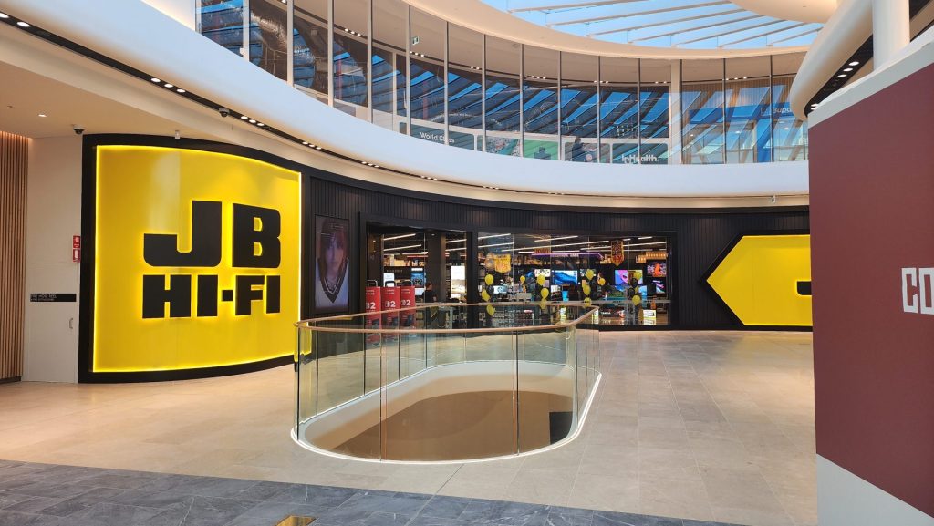 Modern JB Hi-Fi store entrance inside a shopping mall with glass railing and skylight ceiling.