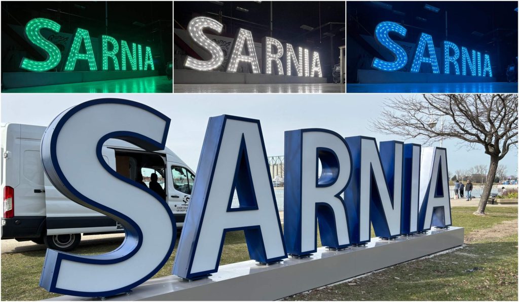 Large 3D letters spelling "SARNIA" shown outdoors in daylight and indoors lit up in green, white, and blue colours.
