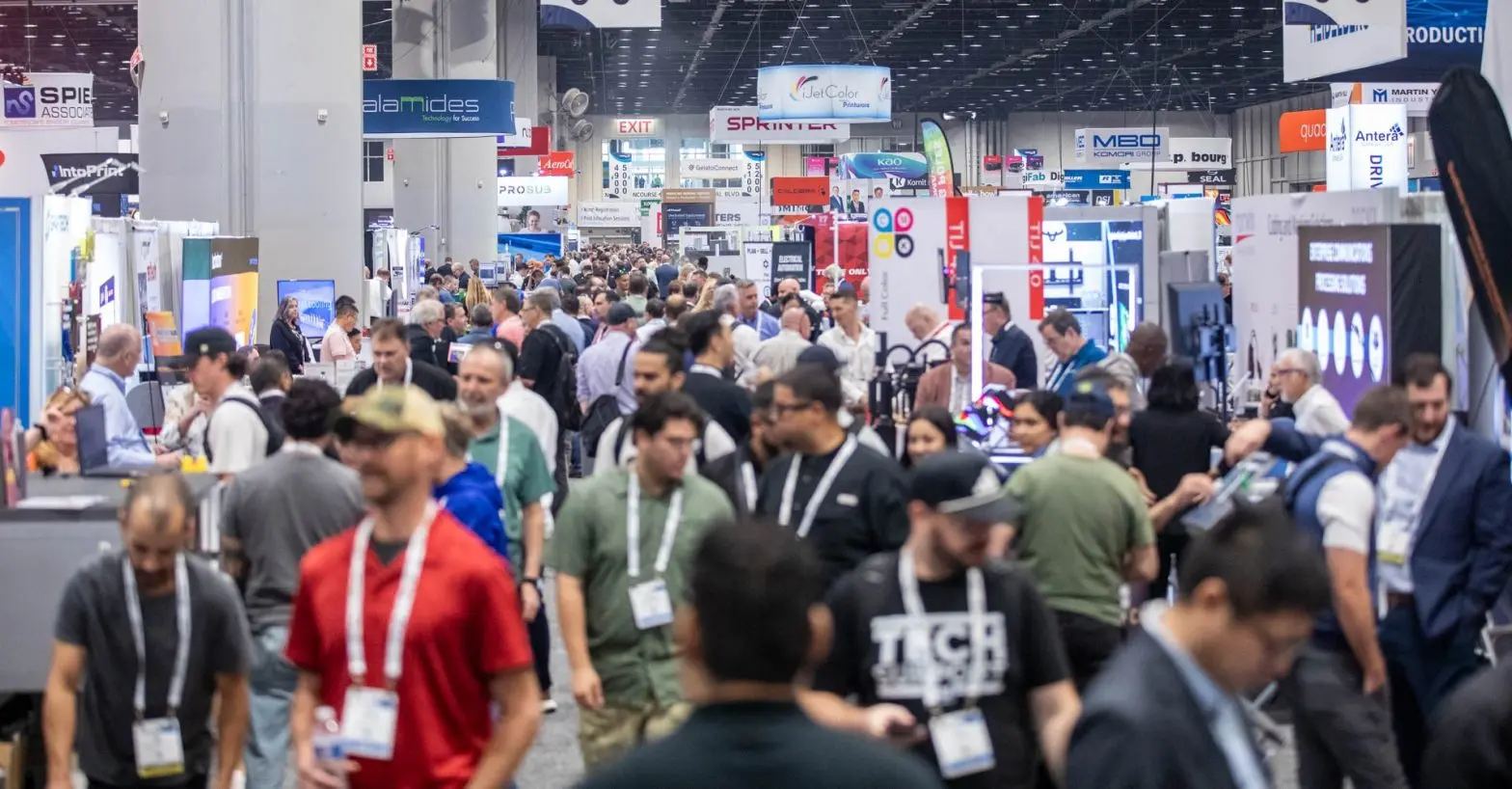 Crowded convention hall with numerous booths and attendees walking and exploring exhibits at the PRINTING United Expo.
