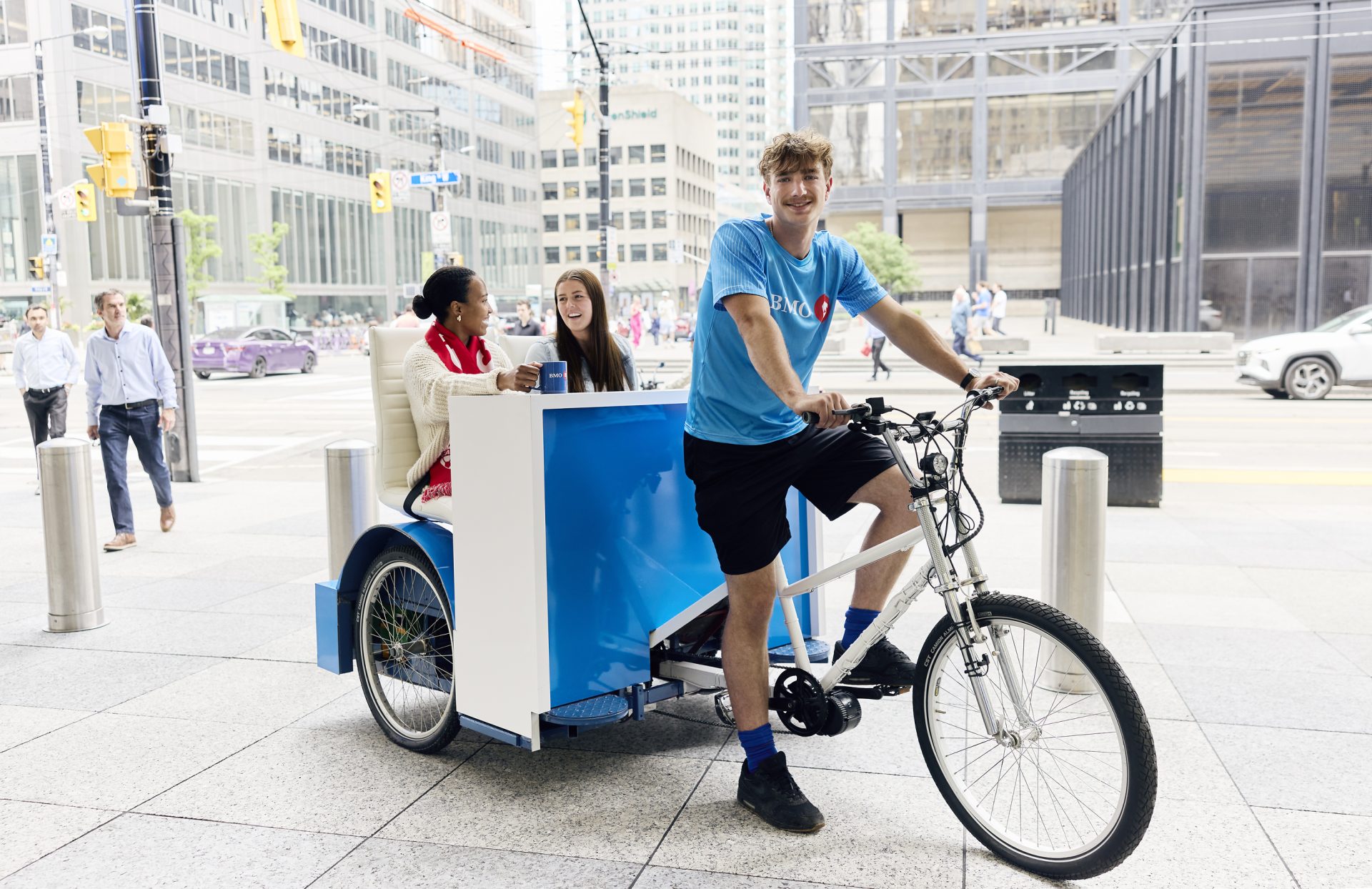 BMO-branded pedicab with rider in BMO shirt and two passengers on a downtown Toronto street.