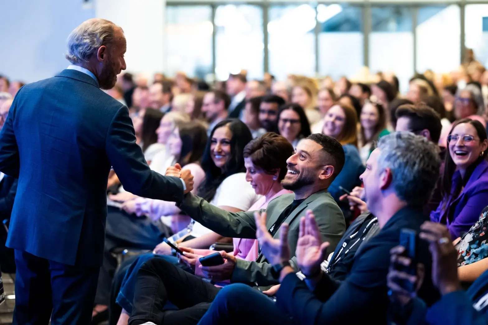 Barry Frey of DPAA fist-bumping an attendee at the DPAA Canada Summit, surrounded by an audience seated in a conference hall at MaRS Centre.