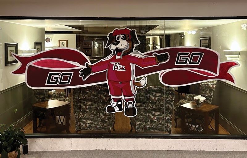 A cartoon dog mascot in a red Petes uniform holds a "Go Go" banner painted on a glass storefront window.