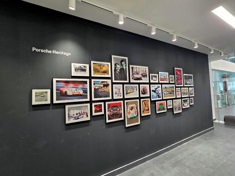 "Porsche Heritage" wall display featuring a curated gallery of framed historic photos and racing images at the dealership.