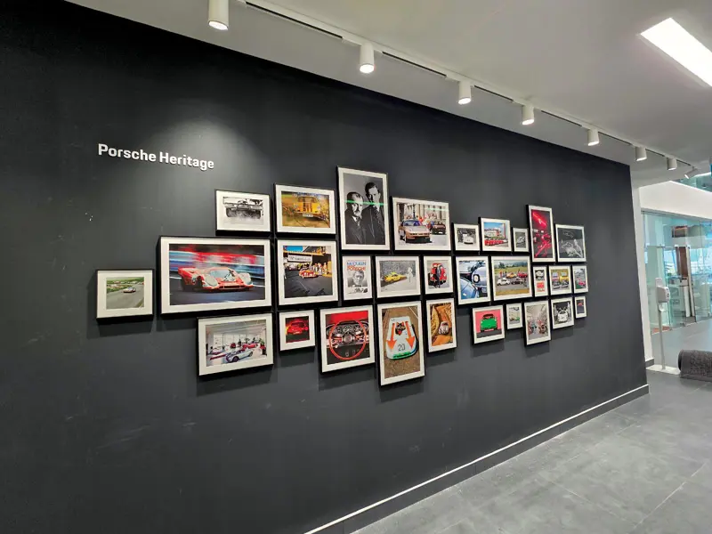 "Porsche Heritage" wall display featuring a curated gallery of framed historic photos and racing images at the dealership.
