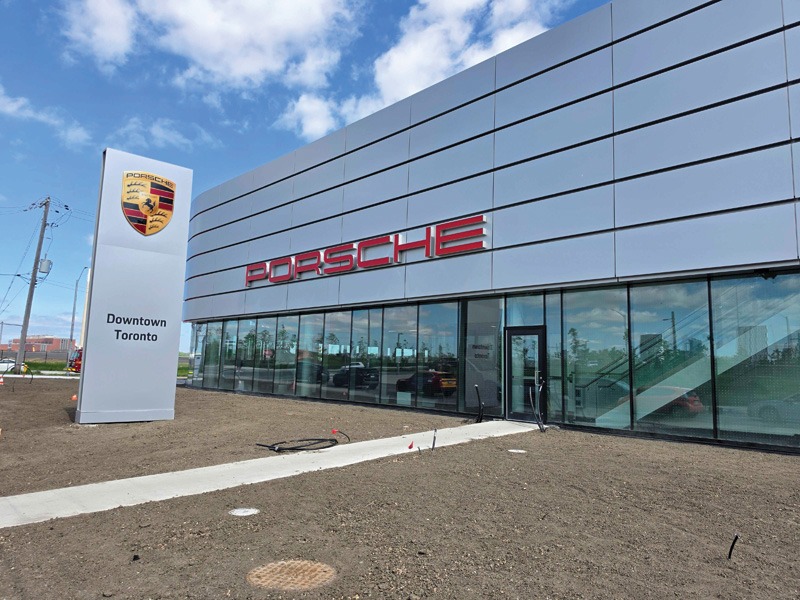Exterior of the Porsche Downtown Toronto dealership showing the illuminated red wordmark, crest pylon sign, and glass facade.