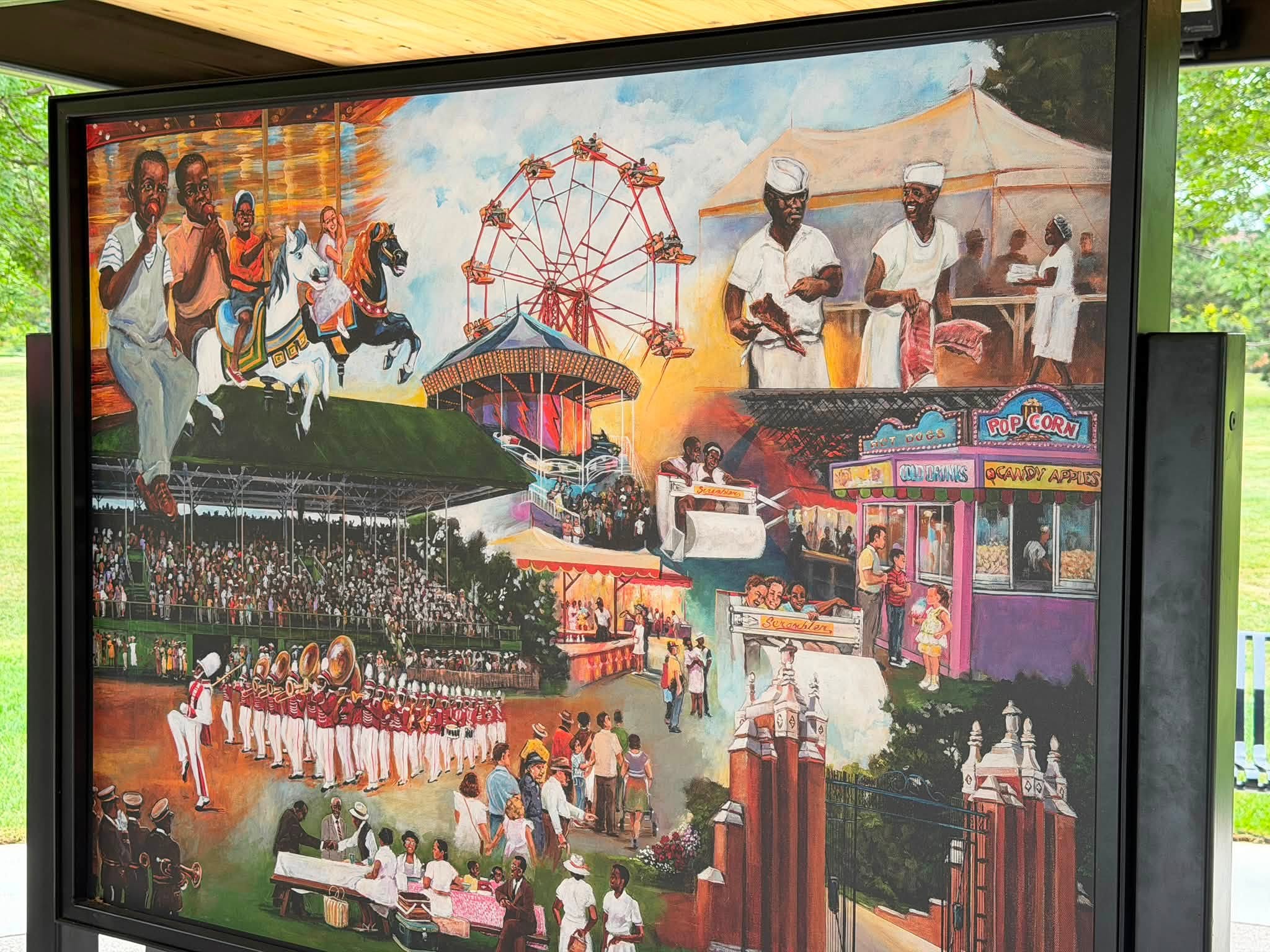 Painted mural depicting a historical fairground scene with a carousel, Ferris wheel, marching band, food stands, and Black families enjoying the fair.